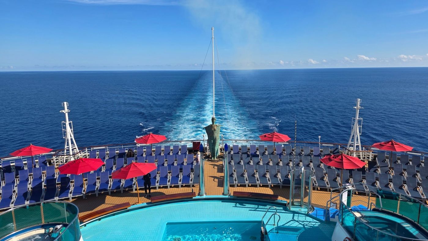 Cruise ship stern deck with red umbrellas, a pool and the wake stretching to the horizon
